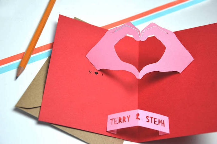ein briefumschalg und eine rote pop up karte mit zwei gebastelten violetten händen aus papier und ein kleiner oranger bleistift, eine pop up karte basteln aus papier