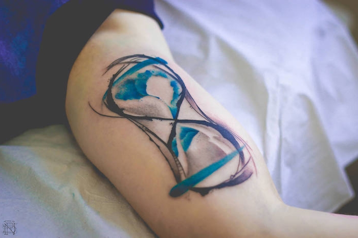 ein bett und eine hand mit einem großen tattoo mit einem farbigen watercolor sanduhr tattoo, eine große tätowierung mit einer großen schwarzen sanduhr mit einem blauen wasser, sanduhr bedeutung 