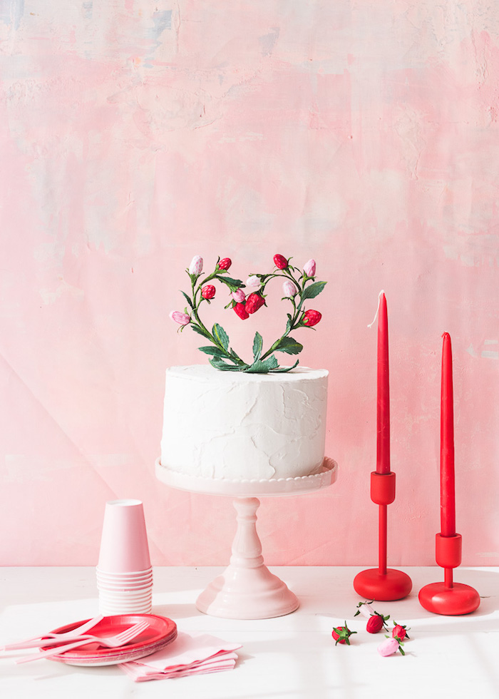 Torte mit Sahne, Herz aus Erdbeeren als Dekoration, rote Kerzen und Teller, rosa Becher und Gabeln