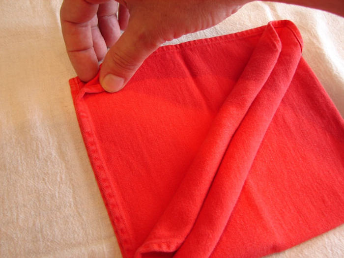 eine hand und eine gefaltete rote bestecktasche, servietten falten anleitung, tischdeko selber machen 