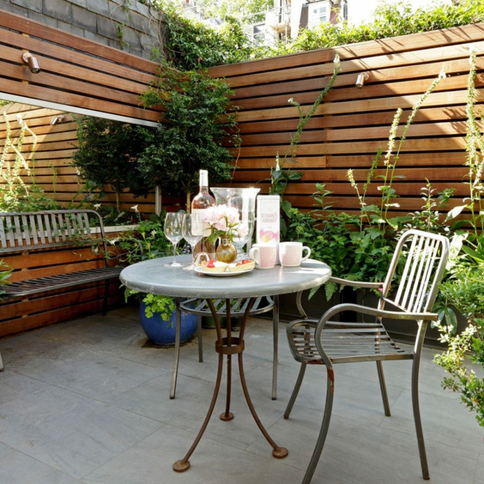 Garten verschönern, hoher Sichtschutz mit Pfanzen darüber, ein gedeckter Tisch, Pflanzkübeln