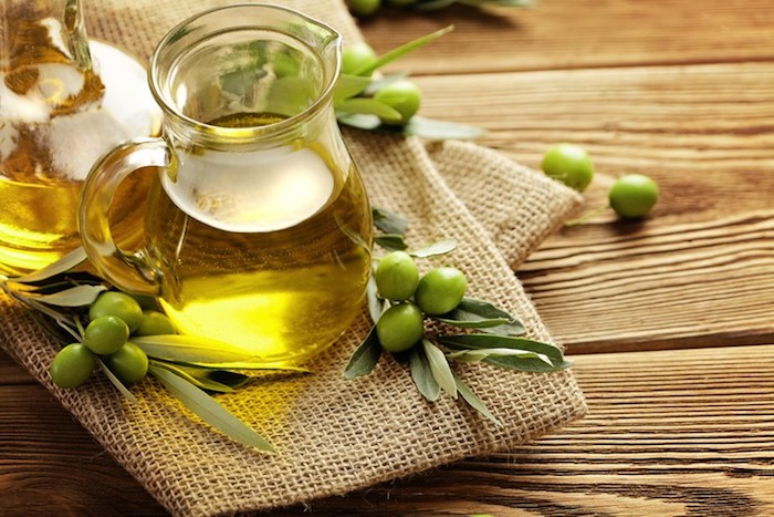 olivenöl haare, grüne oliven, kanne mit öl, leinen, hölterner tischm grüne blätter