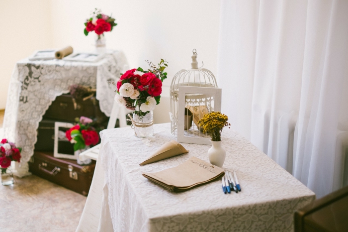 kleine Vase mit Blumen, ein weißer Käfig, weiße Decke mit Blumenmuster, Tischdekoration Kommunion