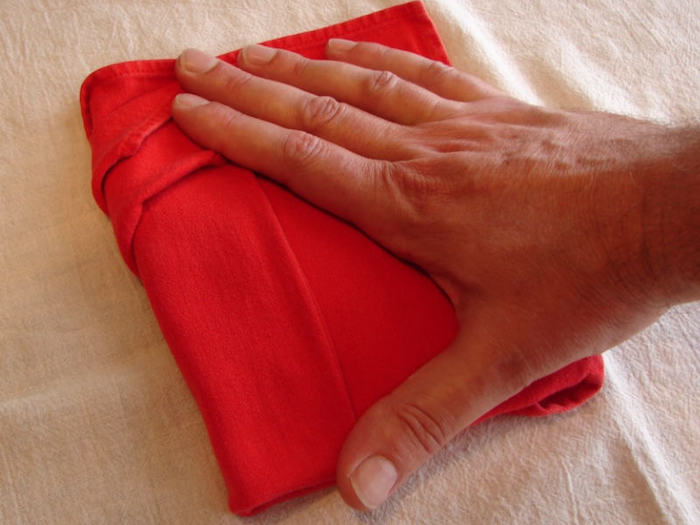 eine hand mit einer kleinen roten gefalteten serviette und eine weiße decke, servietten falten anleitung
