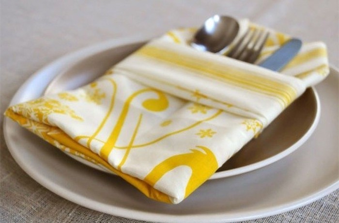 ein tisch mit zwei großen weißen tellern mit einer gefalteten gelben serviette, eine bestectasche mit einem messer, einer gabel und einem löffel, tischdeko selber machen