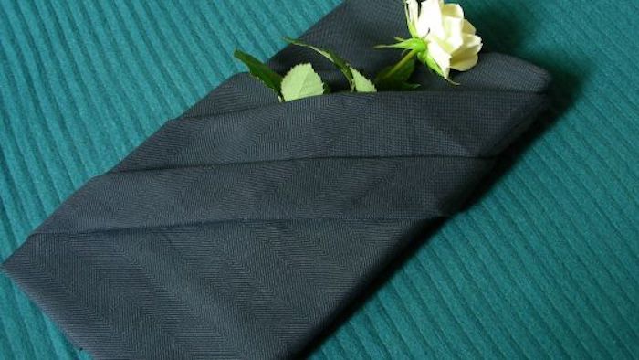 ein tisch mit einer grünen decke und mit einer großen schwarzen gefalteten serviette, eine schwarze bestecktasche mit einer weißen rose mit grünen blättern