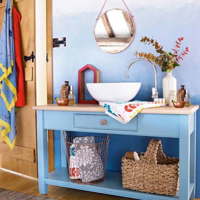 Badezimmer in Blau-Nuancen, weißes Waschbecken, Rattankorb und Badeaccessoires