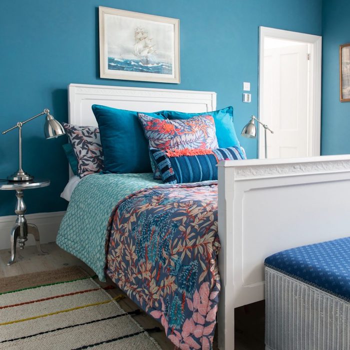 Wandfarbe Blau, weiße Möbel, Kissen und Bettwäsche mit Blumenmuster