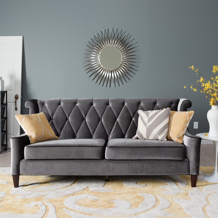 wandfarbe hellgrau mit einem schönen spiegel als deko, großes graues samt sofa mit kissen zum dekorieren und gelbe blumen in weißer vase