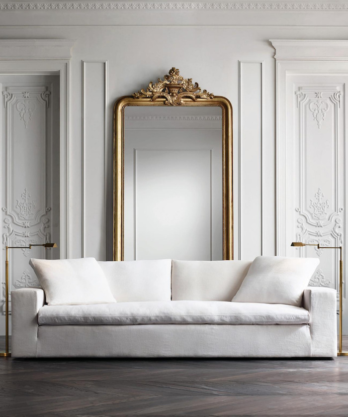 Wandfarbe Weiß, großer Spiegel mit goldenem Rahmen, weißes Sofa und Stehlampen