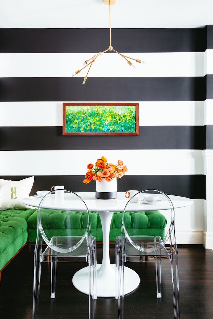 Wandfarbe Schwarz und Weiß, grünes Sofa, durchsichtige Stühle und weißer runder Tisch