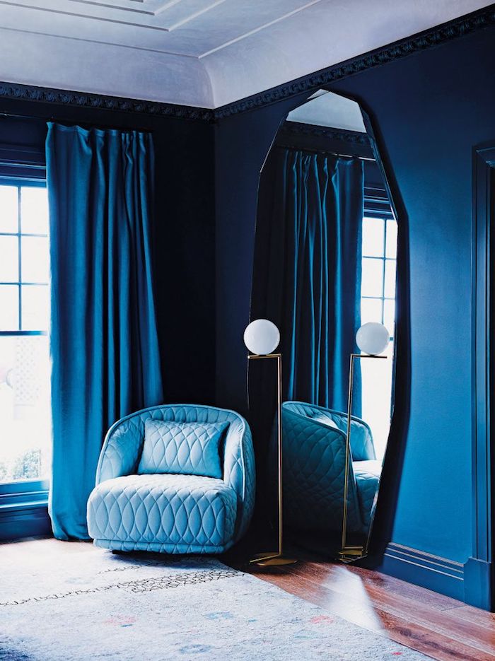 Wandfarbe Dunkelblau, großer Spiegel an der Wand, hellblauer Sessel, blaue Vorhänge