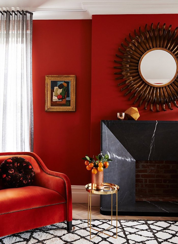 Wohnzimmer in Rot, Spiegel in Form von Sonne, roter Sessel, kleiner Tisch, weiße Vorhänge