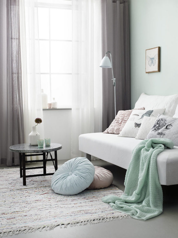 Wohnzimmer in Pastellfarben, Wandfarbe Mintgrün, weißes Sofa mit vielen Deko Kissen, kleiner Couchtisch