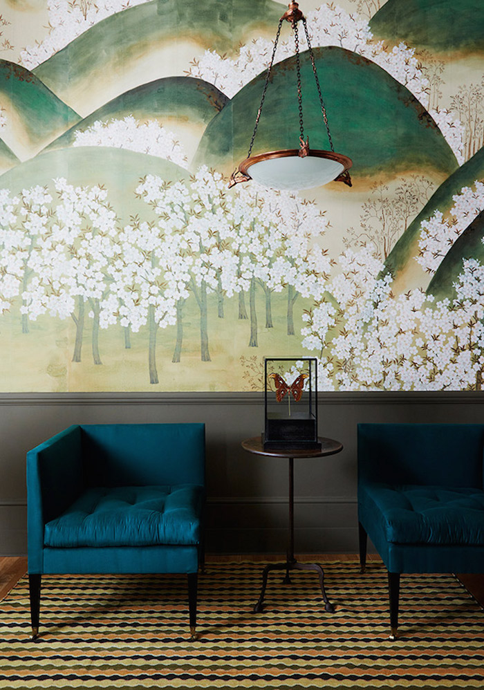 Wohnzimmer Einrichtung, blaugrüne Sessel und kleiner Holztisch, Gemälde an der Wand, Gebirge und blühende Bäume