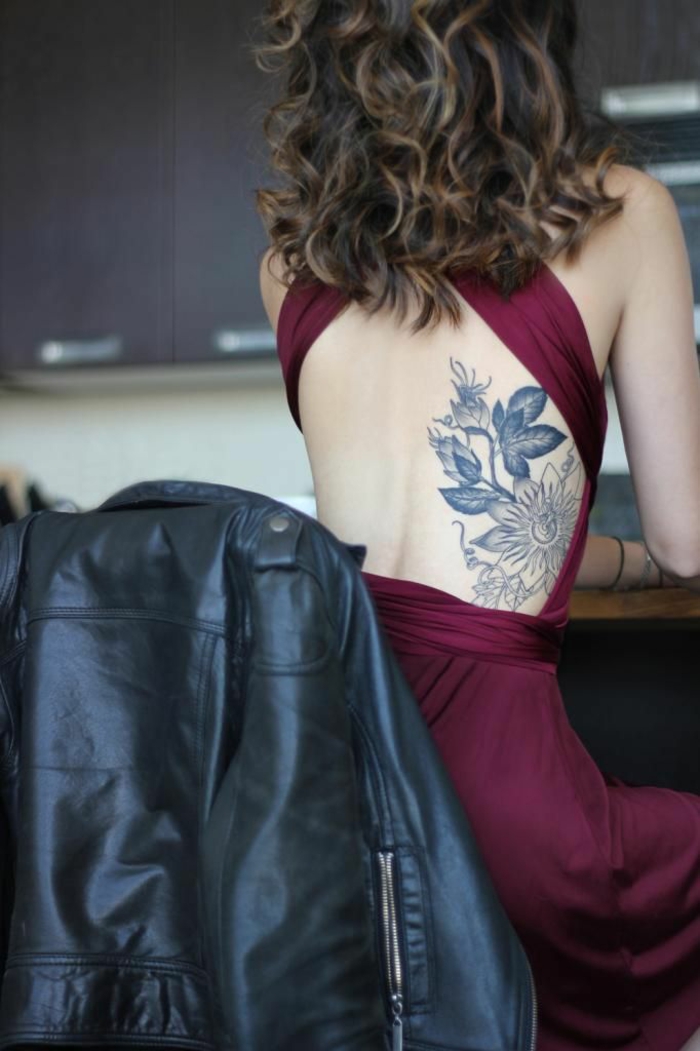 kreatives design von einem blumen tattoo am körper von einer schönen frau, rotes kleid, lockige haare, rückentattoo