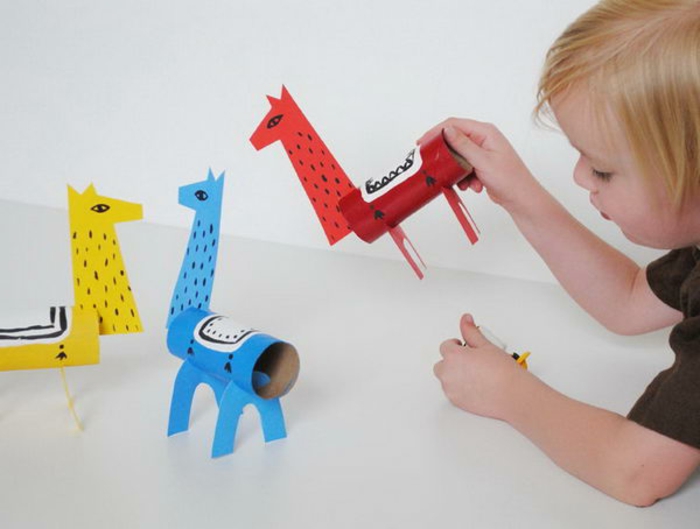 das Kind spielt mit drei Giraffen, Blau, Rot und Gelb, was kann man aus Klopapierrollen machen