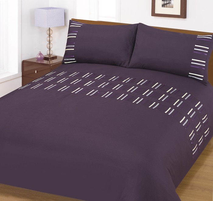 ein schlafzimmer einrichten, ein groes violettes bett mit einer violetten decke und mit zwei großen violetten kissen, aubergine farbe schlafzimmer, eine kleine weiße lampe und ein boden aus holz 