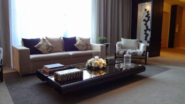ein grauer Teppich, ein niedriger schwarzer Tisch, blaue Kissen, Wohnzimmer Design