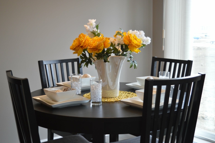 ein Esstisch in schwarzer Farbe, weiße und gelbe Blumen in einer Vase, Grautöne