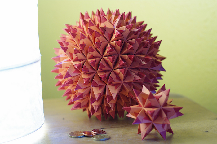 eine lampe und ein tisch aus holz, eine große pinke origami kugel aus papier und ein pinker bascetta stern mit pinken strahlen aus holz