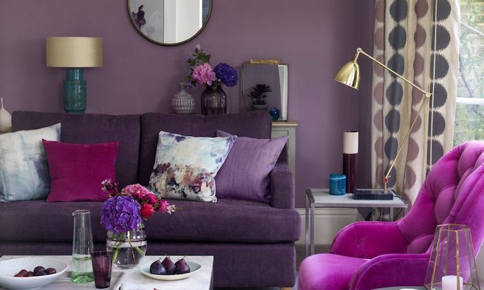 ein wohnzimmer gestalten mit violetten sofas und einer violetten wand, ein kleiner weißer tisch und violette, pinke und rote blumen, eine lampe undeine violette wand mit einem spiegel, aubergine farbe kombinieren