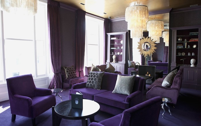 ien wohnzimmer mit kleinen schwarzen tischen und mit violettten sofas mit grauen kleinen kissen, farbe aubergine kombinieren,n große fenster mit violetten gardinen und große gelbe lampen, wohnzimmer einrichten