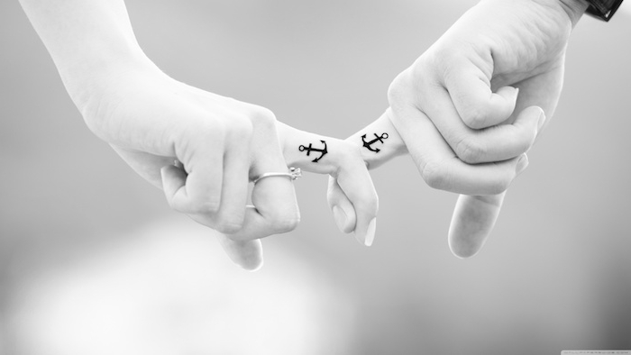 zwei hände mit kleinen schwarzen anker tattoos und mit einem ring, kleine partnertattoos, eine hand mit einem weißen nagellack