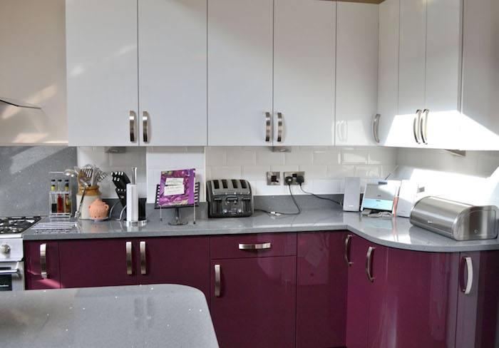 eine küche mit weißen und violetten küchenschränken, schwarzen messern und einem waschbecken, eine güche einrichten, aubergine farbe