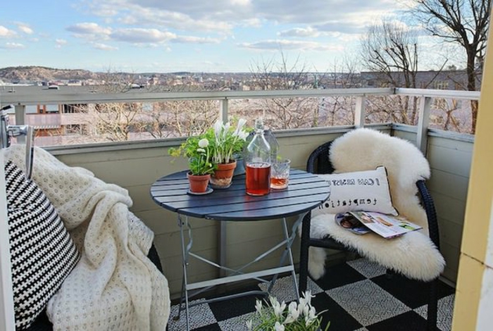 sitzecke balkon gemütlich mit den dekorationen: fellteppich, frische blumen, decke gegen kälte, kissen, kaffeerisch mit wein und schöne aussicht
