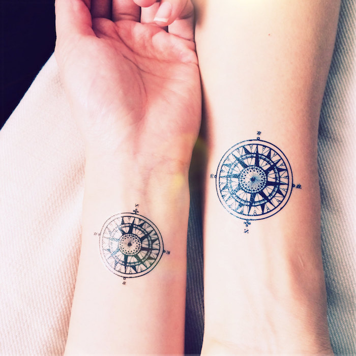 zwei hände mit kleinen schwarzen compass tattoos mit schwarzen pfeilen am handgelenk