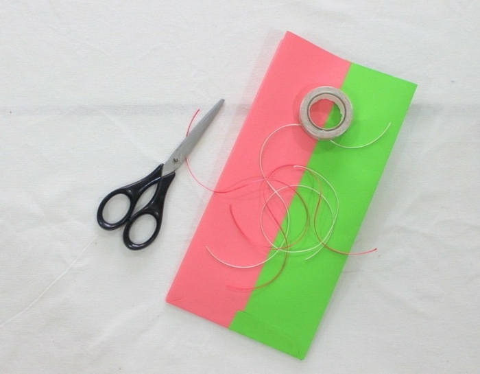 Klebstoff, eine Schere, kleine Papierstreifen, kleine Geschenktüten in Rosa und Grün