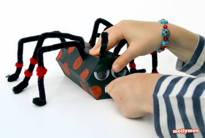eine schwarze Spinne mit roten Flecken, das Kind spielt mit der Spinne, Basteln mit Klorollen