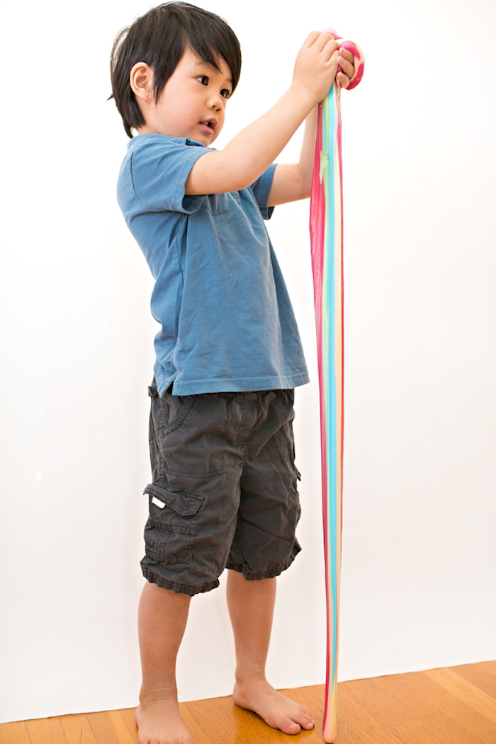 Süßes Kind spielt mit Regenbogen Schleim, verschiedene Farben, blaues Shirt und schwarze Hose