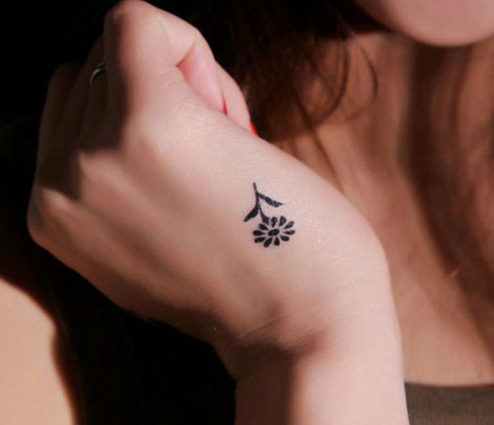 kleine und dezente blumen tattoo idee an der hand, gänseblümchen in schwarz, kleine tattoos