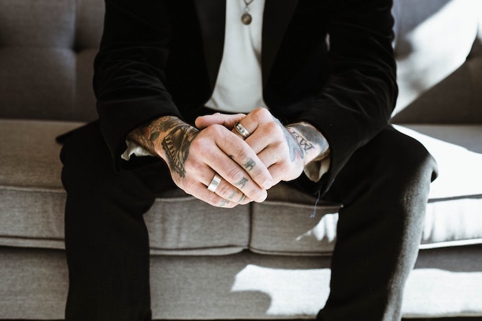 Tattoos an beiden Armen und an Fingern, Mann mit schwarzem Anzug und weißem Hemd