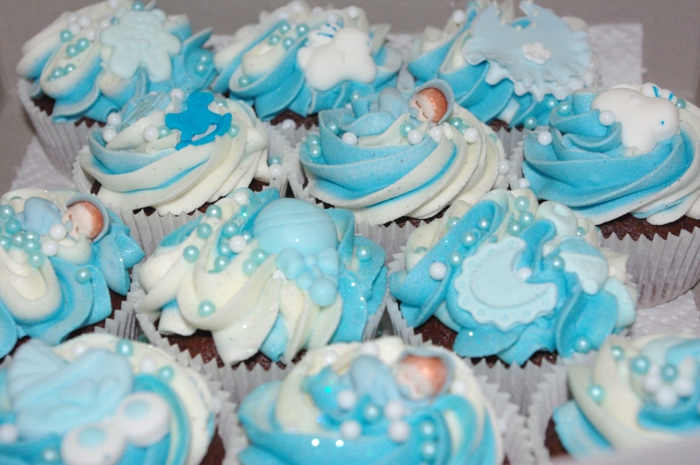 eine Menge Cupcakes mit kleinen schlaffenden Babyfiguren als Dekoration, Perlen, Babyparty organisieren