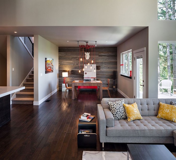 dekoideen wohnzimmer, boden aus dunklem holz, graues sofa mit gelber dekokissen, hängende lampen mit roten kabeln