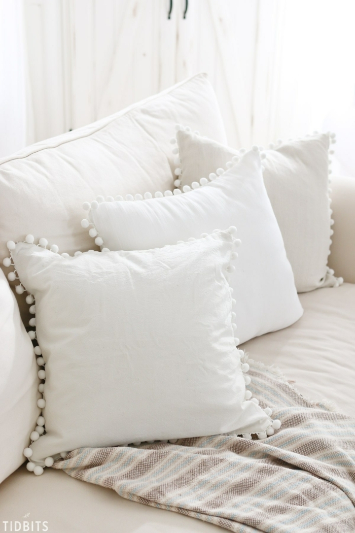 Sofa in weißer Farbe, drei Kissen mit weißen Pompons verziert, Pompons selber machen