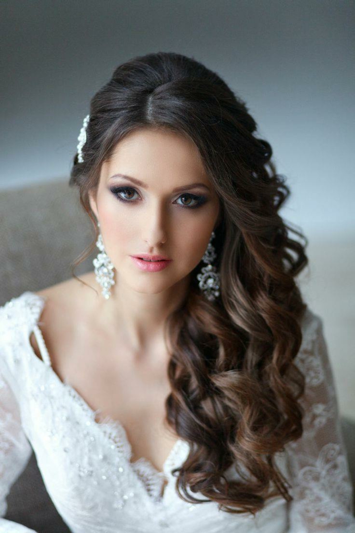 eine schöne Braut mit lockigem Haar, lange Ohrringe, lässige Locken und Haarschmuck