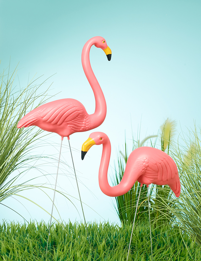 ein blauer himmel und grüne pflanzen, ein garten mit flamingo deko, zwei pinke große flamingos 