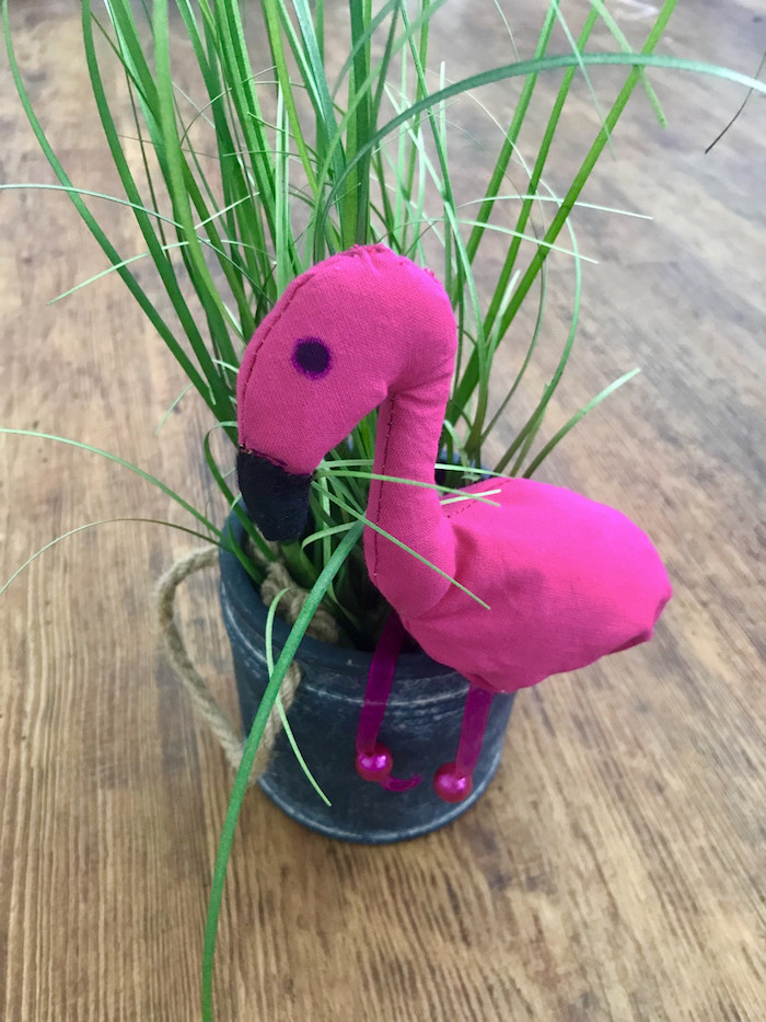 ein blumentopf mit einer grünen pflanze und eine kleine violette dekorative flamingo und ein brauner boden aus holz