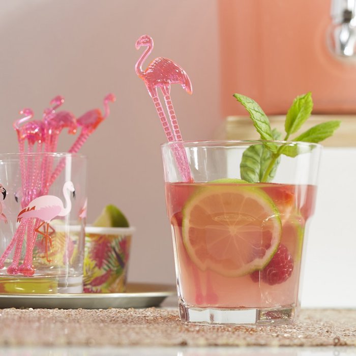 ein glas mit einem pinken cocktail mit einer grünen zitrone und mit pinken flamingo cocktail stäbchen