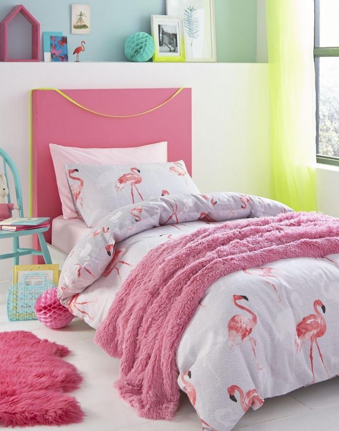 ein kinderzimmer einrichten in flamingo style, ein bett mit einer decke mit vielen kleinen pinken deko flamingos, ein fenstern und ein grüner vorhang, ein weißes kissen mit pinken flamingos und ein blauer stuhl
