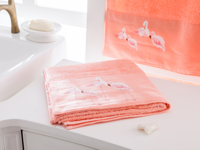 eine kleine weiße seife und ein pinker tuch mit vier weißen flamingos mit pinken und weißen federn und ein spiegel