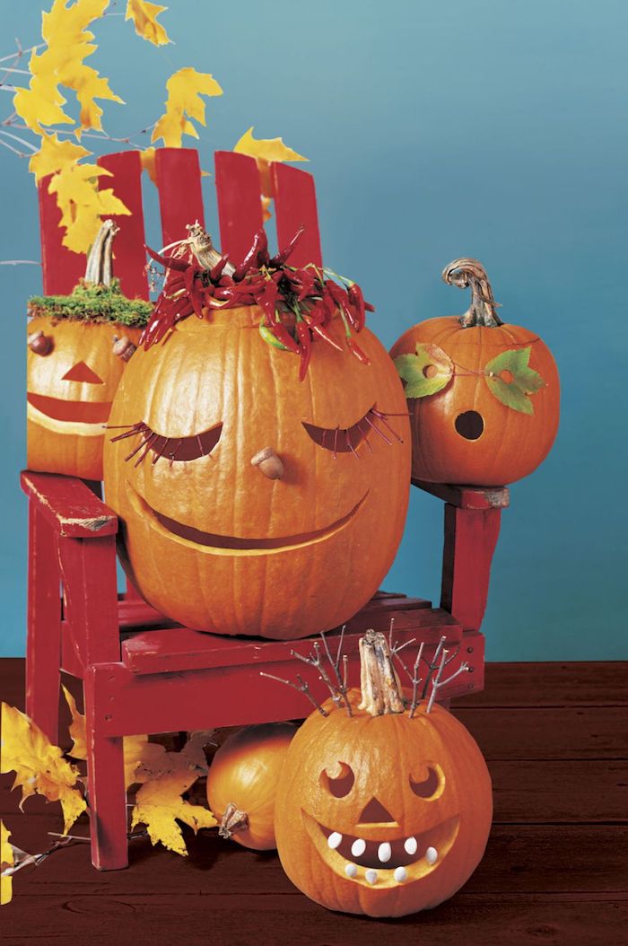 eine blaue wand und ein kleiner roter stuhl aus holz mit kleinen orangen kürbissen mit halloween kürbisgesichtern und vielen gelben blättern, lustige kürbisgesichter schnitzen 