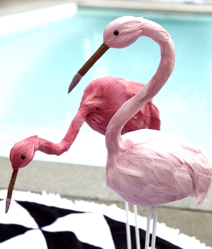 ein kleiner schwarz-weißer teppich und ein blaues schwimmpoool und zwei große pinke deko flamingos mit pinken federn, pink flamingo