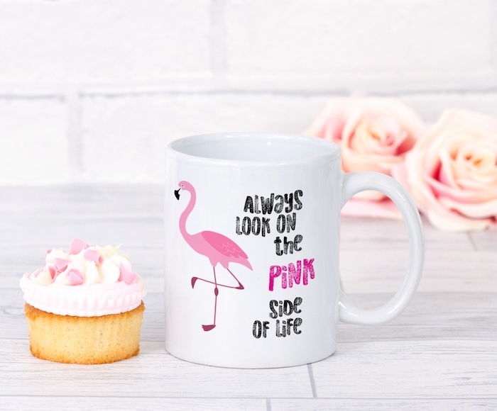 eine weiße tasse mit einer pinken flamingo mit pinken federn und ein weißer tisch aus holz und zwei pinke rosen und ein kuchen mit einer pinken sahne, pink flamigo deko