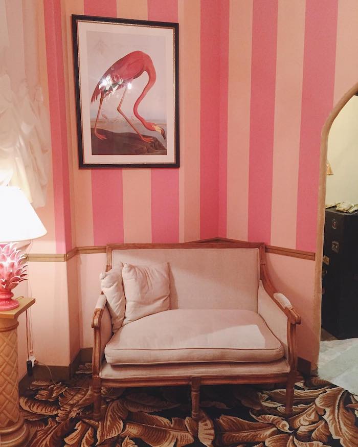 eine weiße lampe und ein weißes sofa mit weißen kissen und eine pinke wand mit einem bild mit schwarzen bilderrahmen, bild mit einer pinken flamingo und ein spiegel 