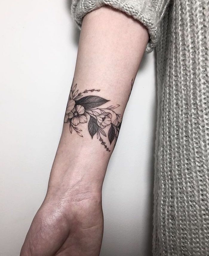 weiße wand und eine junge frau mit einer hand mit einem schwarzen tattoo mit kleinen weißen und schwarzen blumen und schwarzen blättern, frauen tattoos ideen, arm tattoo frau